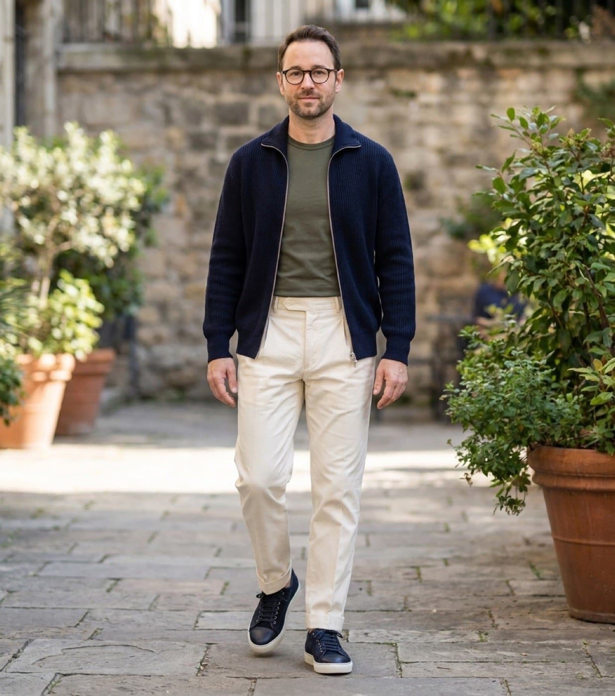 KOTS preview of Rami in navy knitwear, an olive top and cream trousers, walking through a courtyard